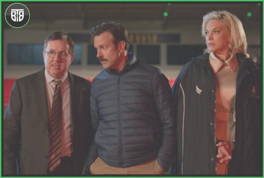 two men are talking each other and a lady is standing near them in Ted lasso, binge worthy tv shows